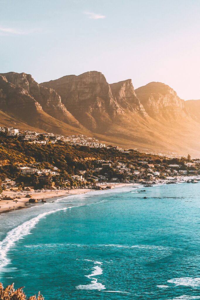 Coastal town along a sandy beach with turquoise water and rugged mountains in the background at sunset. Alt text is concise; conveys setting and mood without unnecessary detail.