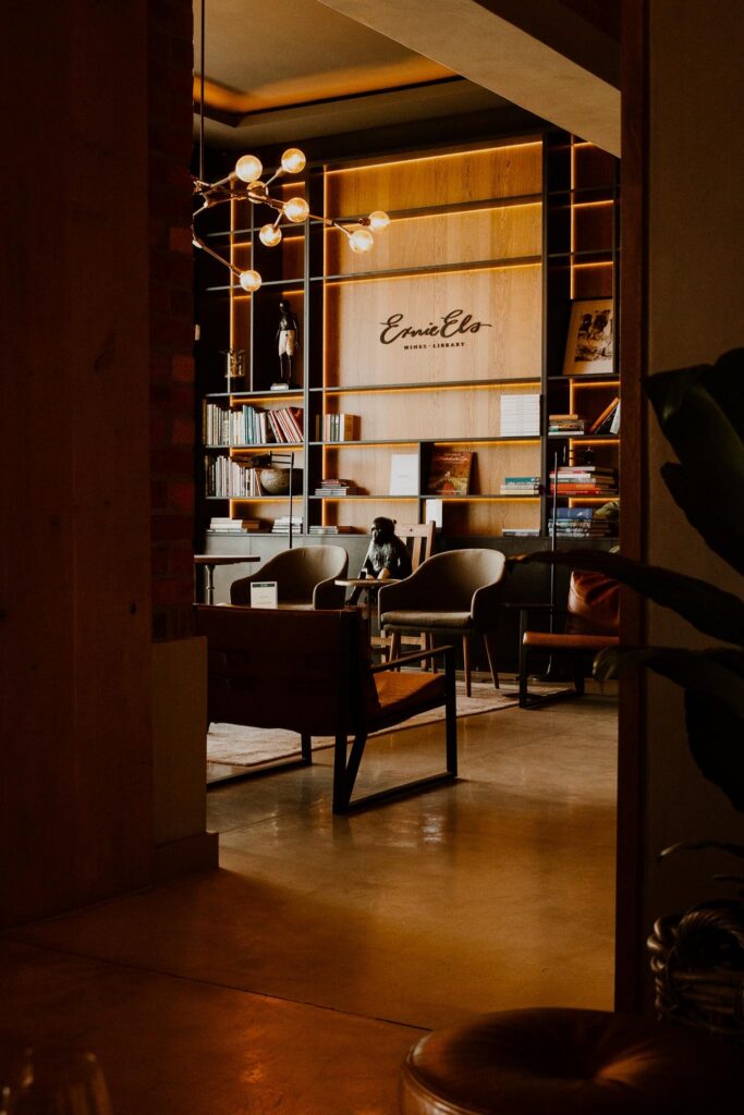 Cozy library lounge with warm lighting, wooden shelves, and mid-century chairs.