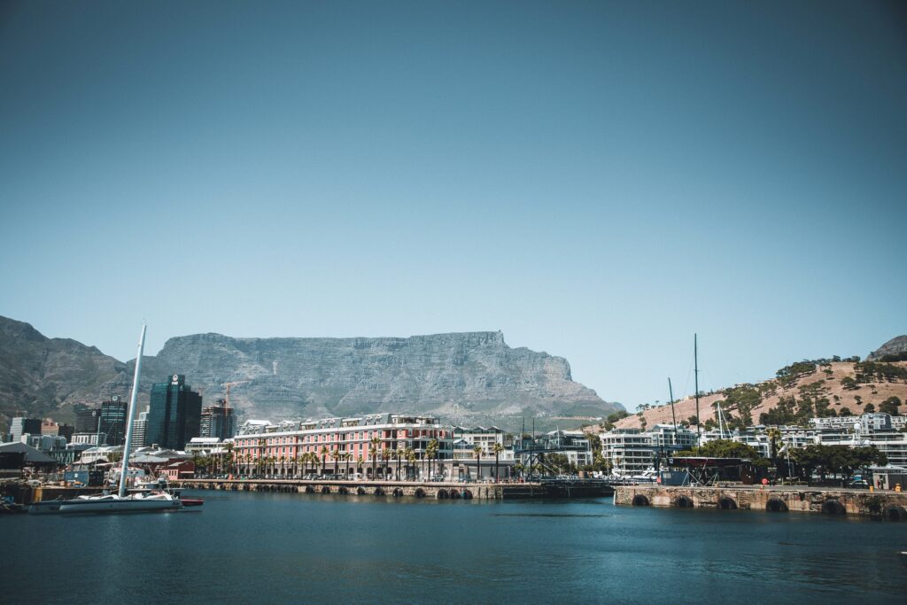 Harbor scene in Cape Town with calm water, a row of pastel waterfront buildings, and Table Mountain in the background.