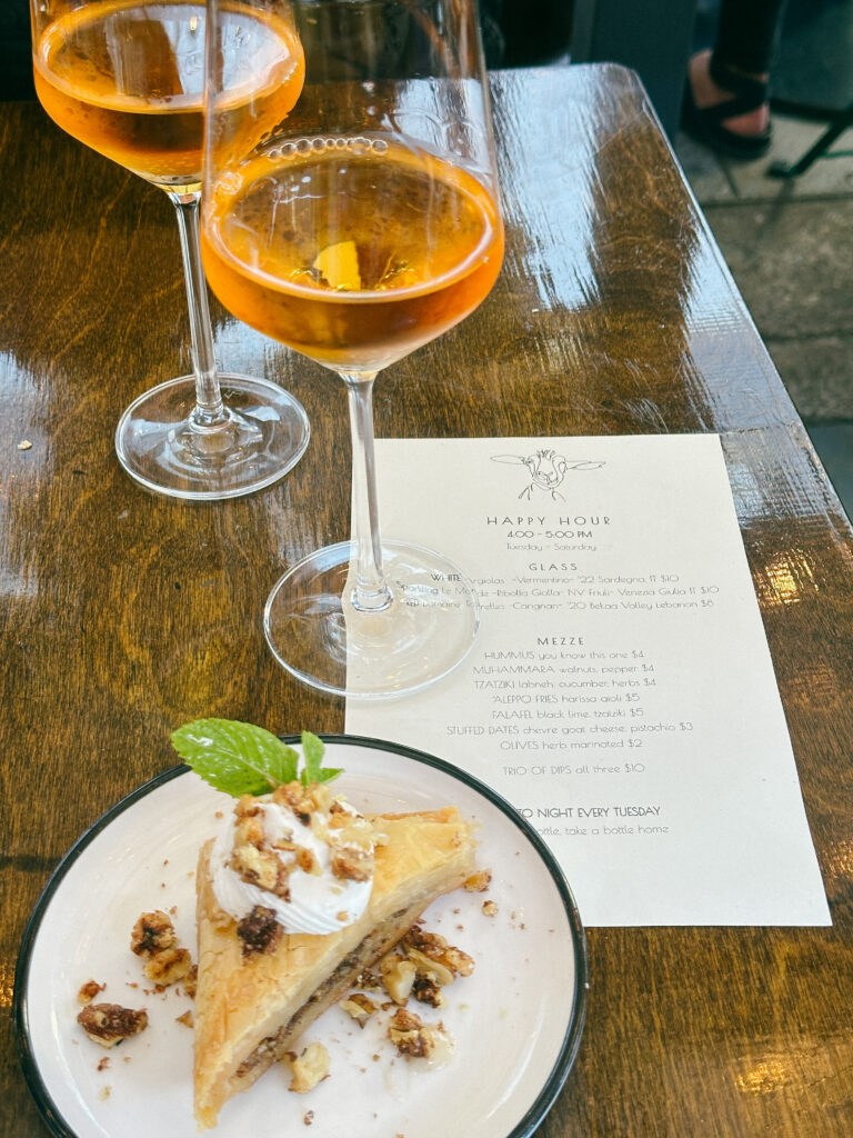 Two orange cocktails in stem glasses on a wooden table, with a menu and a pastry dessert beside them.