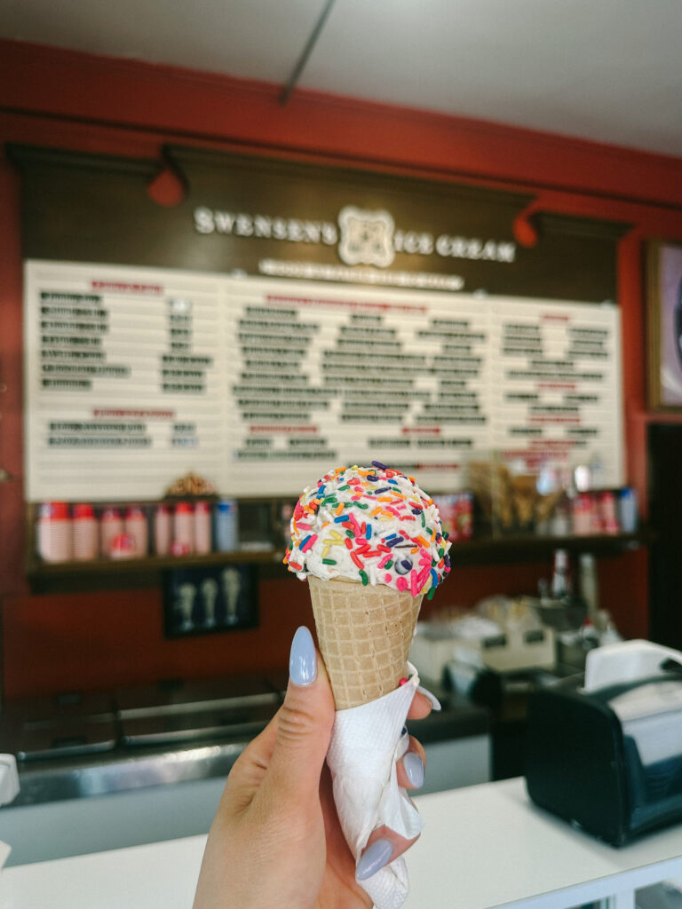 Close-up of a vanilla ice cream cone with rainbow sprinkles held in a napkin at an ice cream shop.