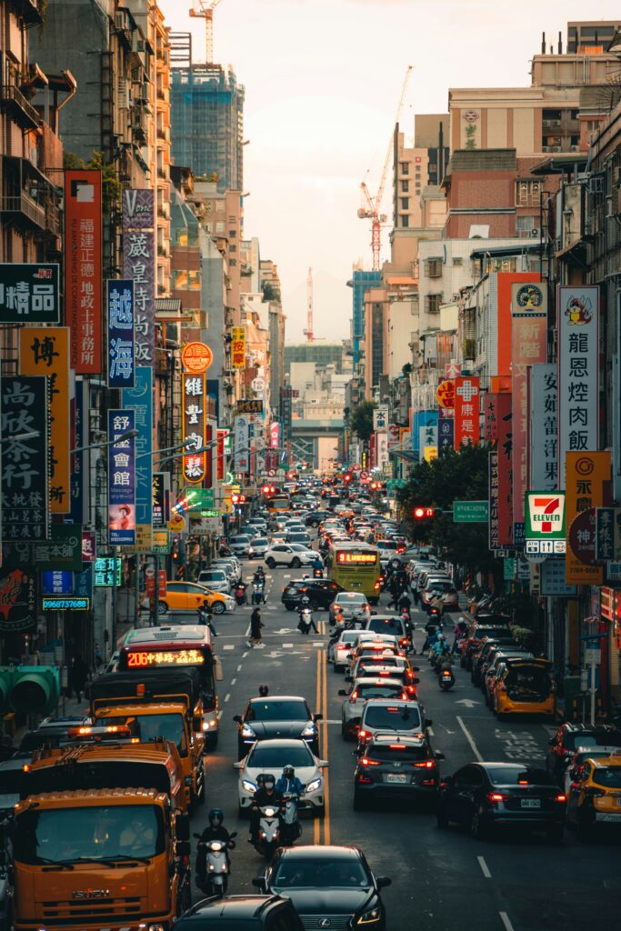 Busy Asian street lined with colorful vertical signs and heavy traffic of cars, buses, and motorcycles at dusk, buildings on both sides.