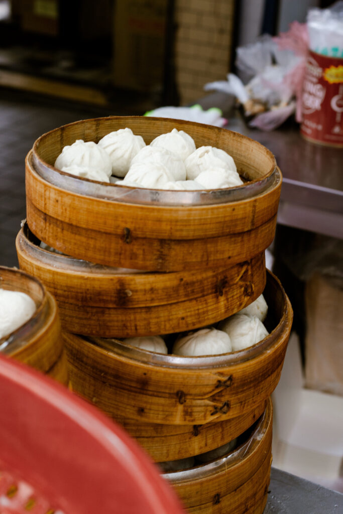 Stack of round bamboo steamers filled with white steamed dumplings (bao) inside.
