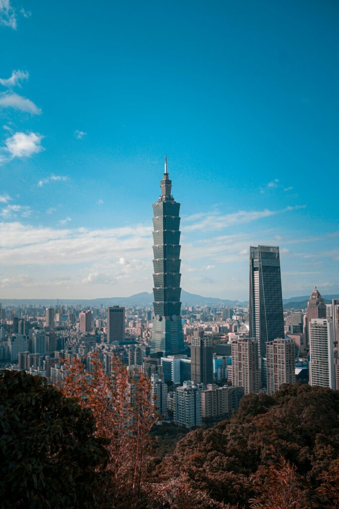 Taipei 101 rising above a dense cityscape under a clear blue sky, with trees in the foreground.