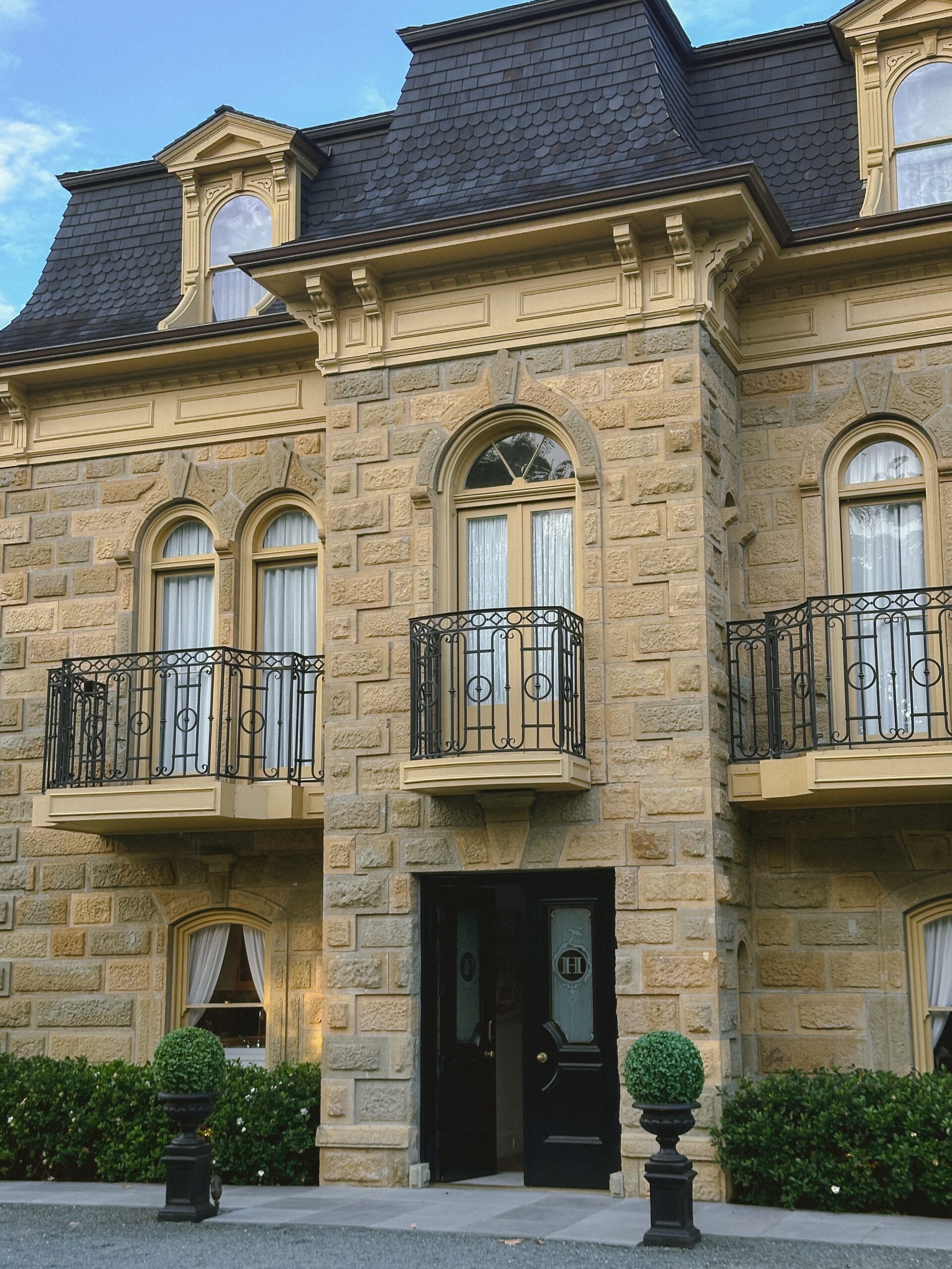 Stone townhouse facade with arched windows, decorative moldings, and wrought-iron balconies above the entrance door.