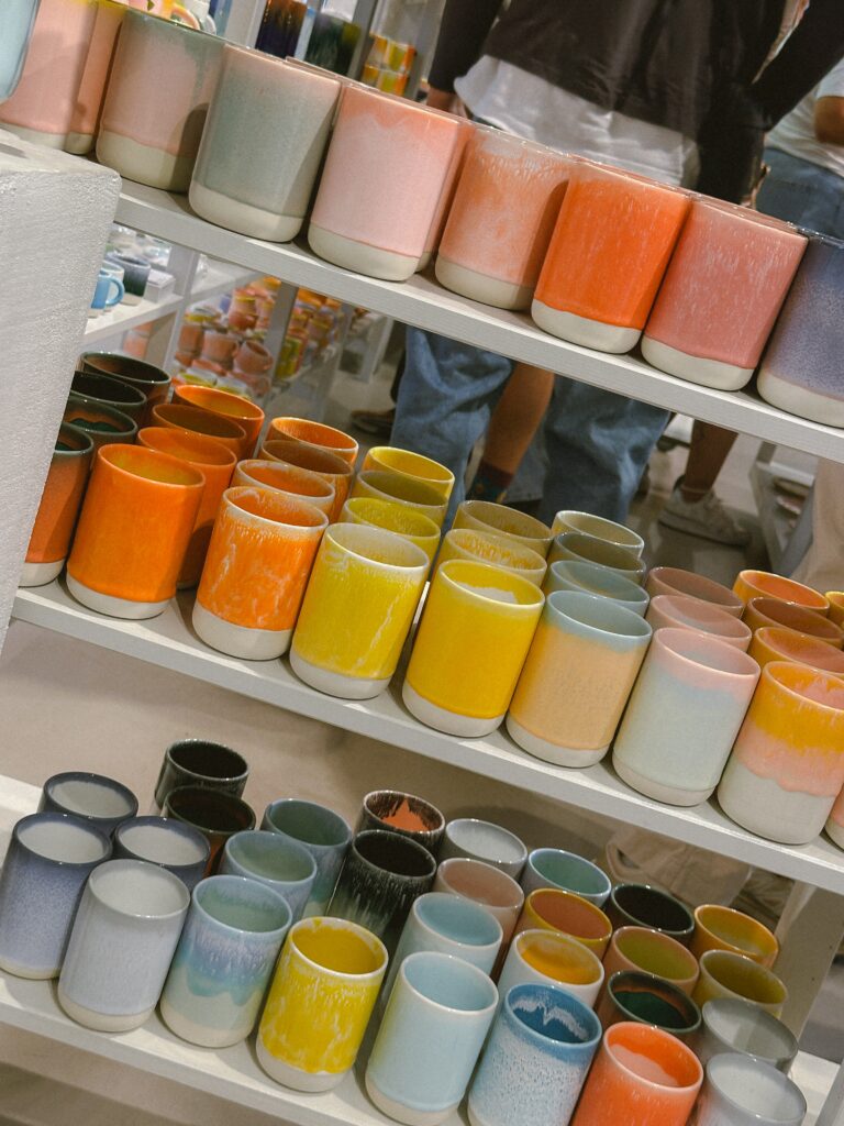 Rows of colorful ceramic mugs on display shelves in a store, showcasing pastel pinks, blues, yellows, and oranges.
