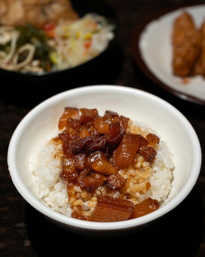 White rice topped with glossy braised pork in a brown sauce, served in a small white bowl.