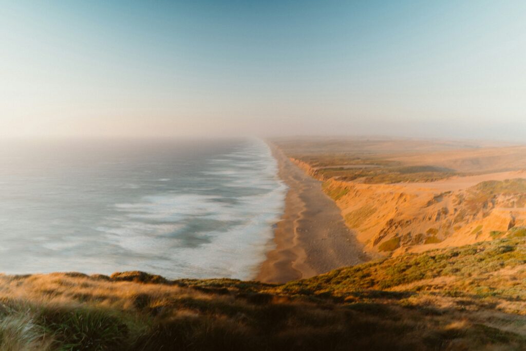 Aerial view of a dramatic sweeping sandy beach and golden cliffs along the Northern California coast at golden hour