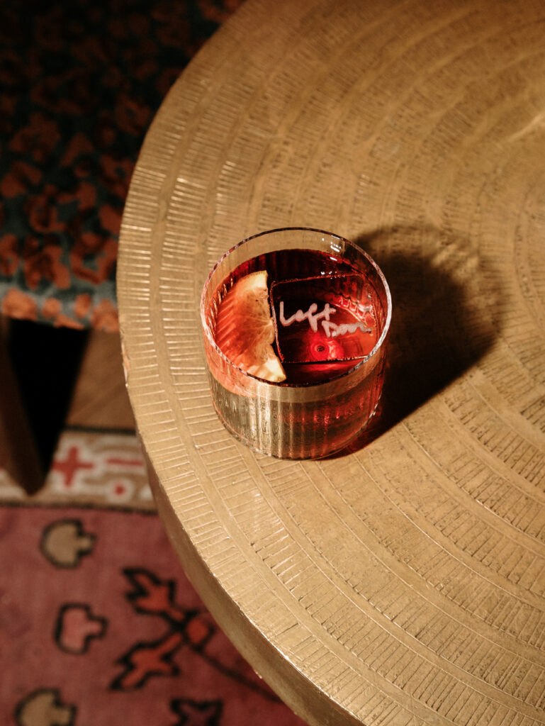 Glass of red drink with a lemon wedge on a round, textured wooden table