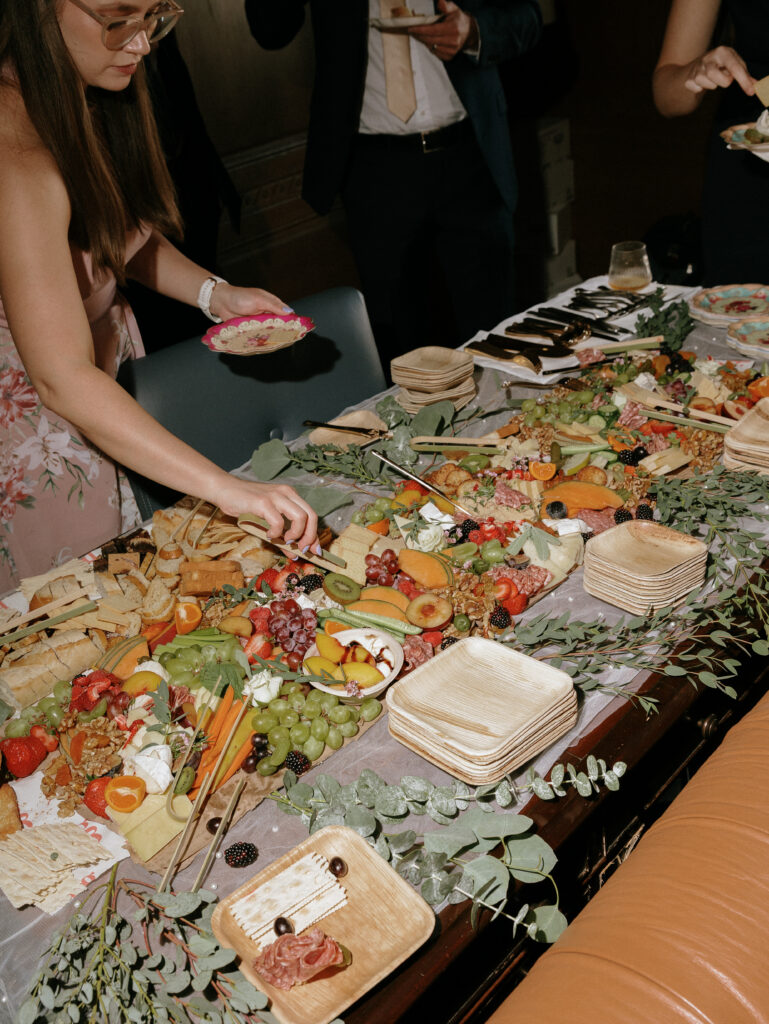 Guests help themselves to a lavish grazing table of fruit, cheese, crackers and greens at a social event.