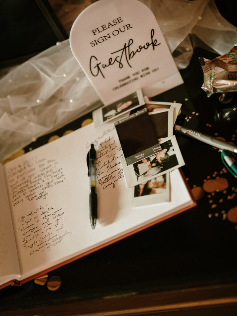Open guest book with handwritten notes, photos, and a pen, ready for guests to sign at a celebration.