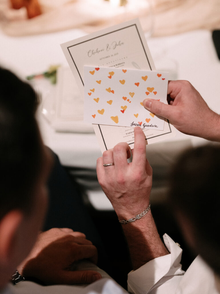 Close-up of a person holding a heart-patterned wedding invitation over a white table surface.