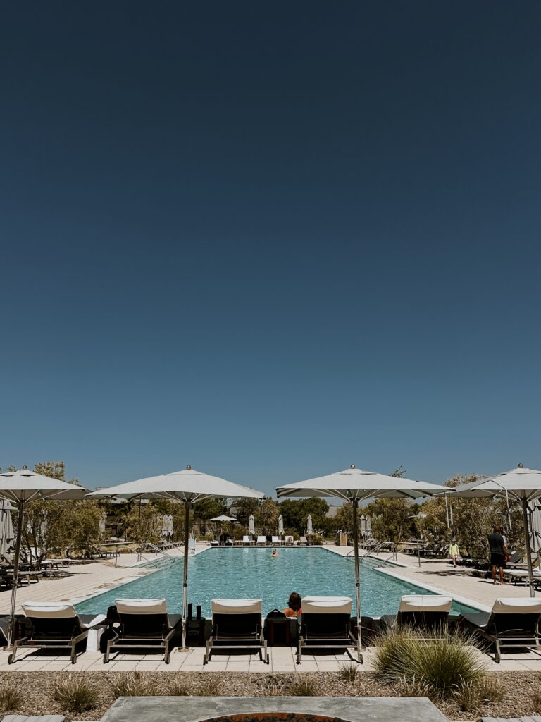 Poolside area with white umbrellas and lounge chairs under a clear blue sky, at a resort.