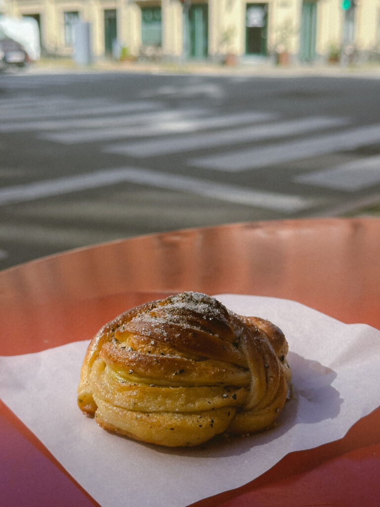 Coiled spiraled baked pastry on white parchment, outdoors on an orange plate with a blurred street background