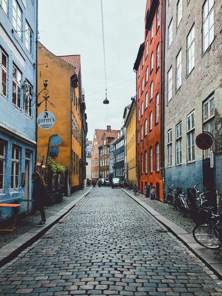 Colorful narrow cobblestone street lined with blue, yellow, orange and red buildings; bicycles parked along the curb.
