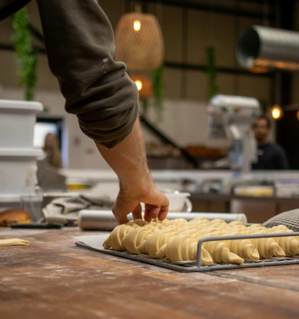Baker's arm shaping twisted dough shapes on a baking rack in a bakery